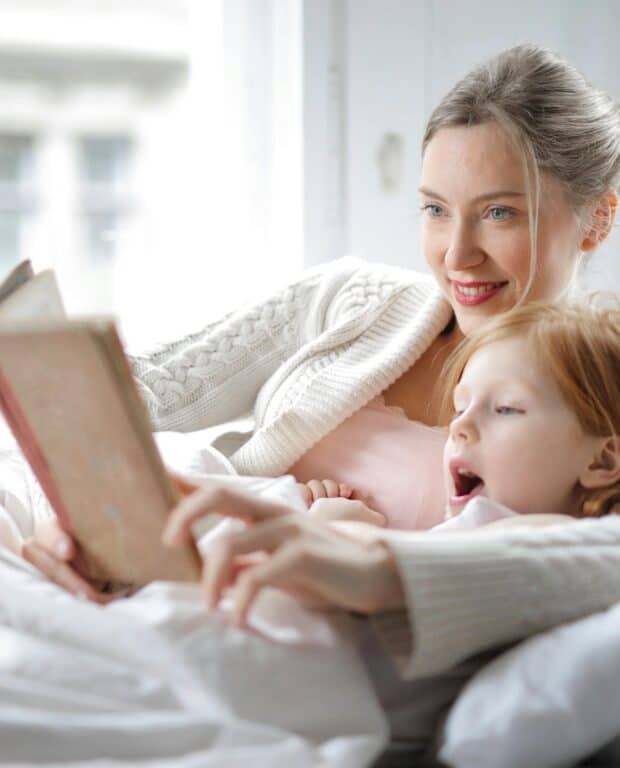 Mother reading to her daughter in bed to establish a healthy sleep routine